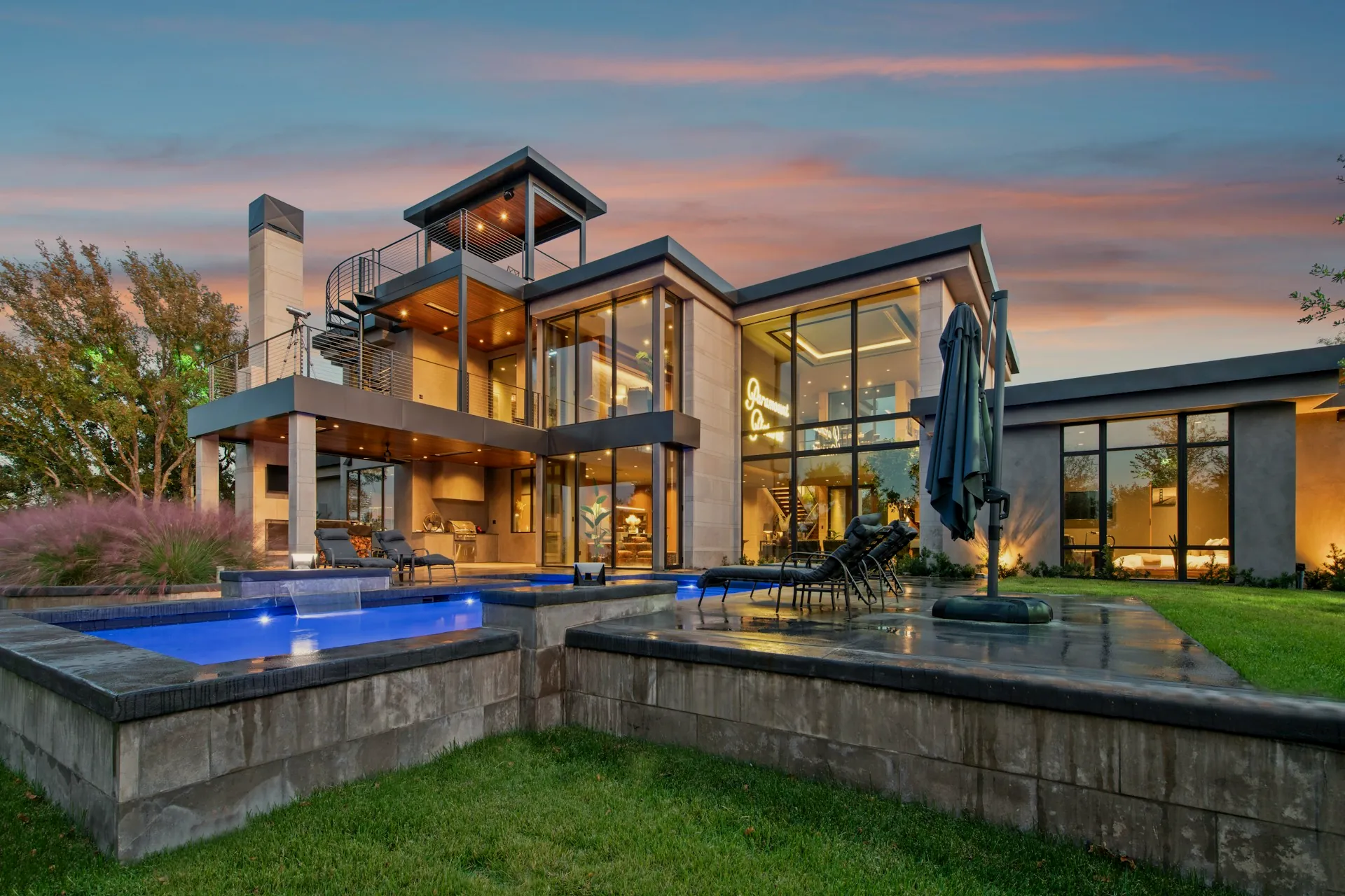 Modern glass mansion illuminated warmly against the dusk sky